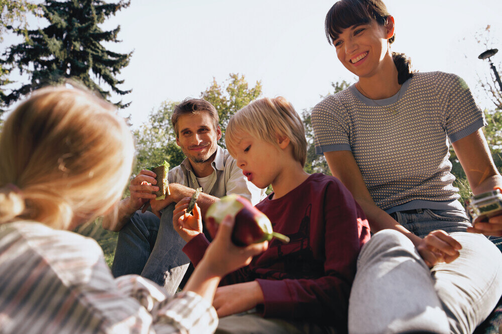 Junge Familie sitzt im Freien und isst Brot sowie Äpfel